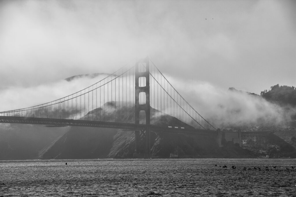 This image is a black-and-white photo of the Golden Gate Bridge. The bridge is shrouded in fog, restricting its visibility to the viewer.