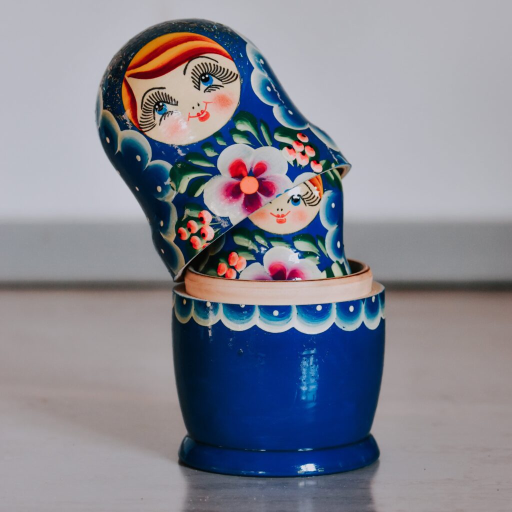 This image is a photo of a set of blue Russian dolls. The outer doll is partially split open, revealing half the face of the doll within it.